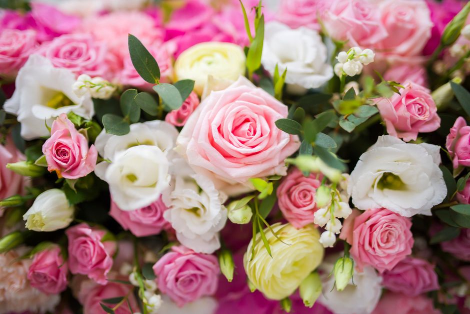 A close-up view of a floral arrangement featuring a variety of fresh flowers, including soft pink roses with tightly wound petals, creamy white lisianthus with delicate, ruffled petals, and small whit