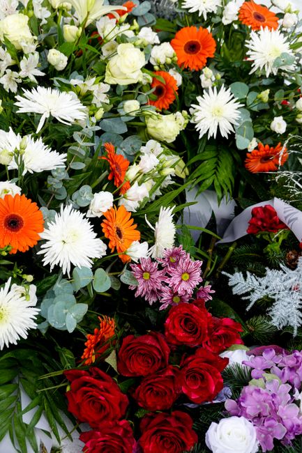 A vibrant floral arrangement featuring an assortment of fresh flowers, including bright orange gerbera daisies, white chrysanthemums, delicate pink chrysanthemums, deep red roses, and white lisianthus