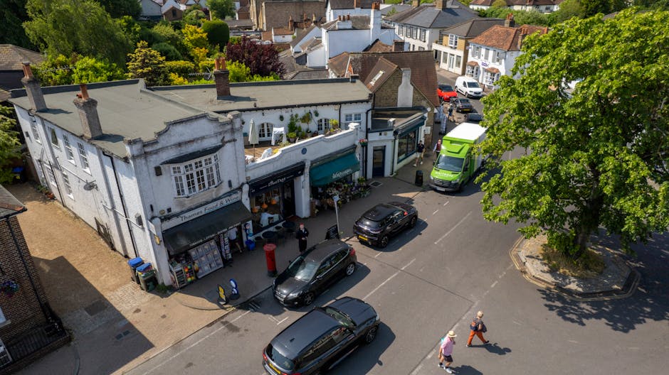 An aerial view of a charming flower shop located on Epsom High Street, featuring a white building with large display windows and a teal awning. The shop, associated with flower delivery services in Ep